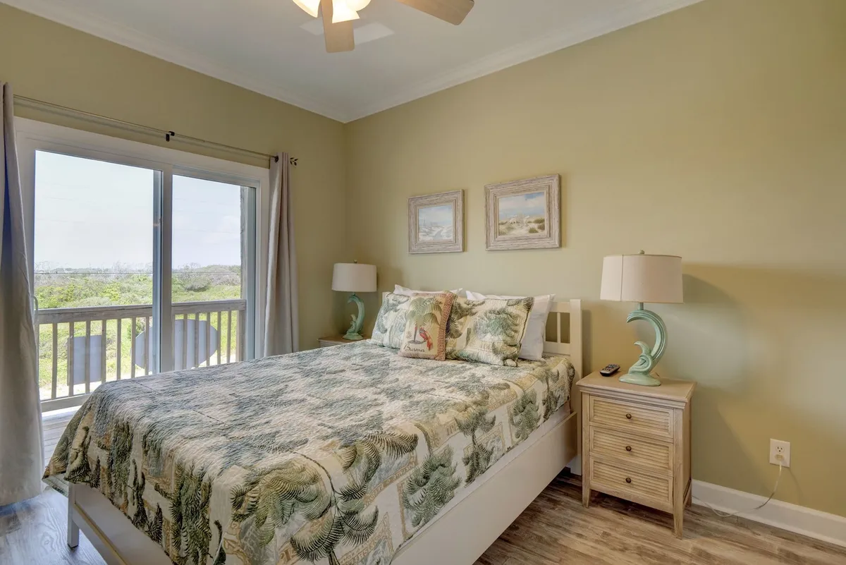 A cozy bedroom featuring a bed with patterned bedding, a sliding glass door that opens to a beautiful view, a unique lamp, and framed artwork. The room is filled with soft light, exuding comfort and a serene retreat ambiance.