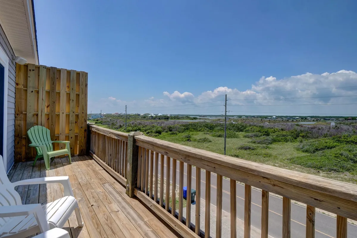 An exterior view featuring a wooden deck outfitted with classic Adirondack chairs, looking out over a tranquil natural landscape. The openness and comfort of the seating area suggest a perfect spot for sipping coffee at sunrise, enjoying cocktails at sunset, or simply relaxing together in the fresh air.