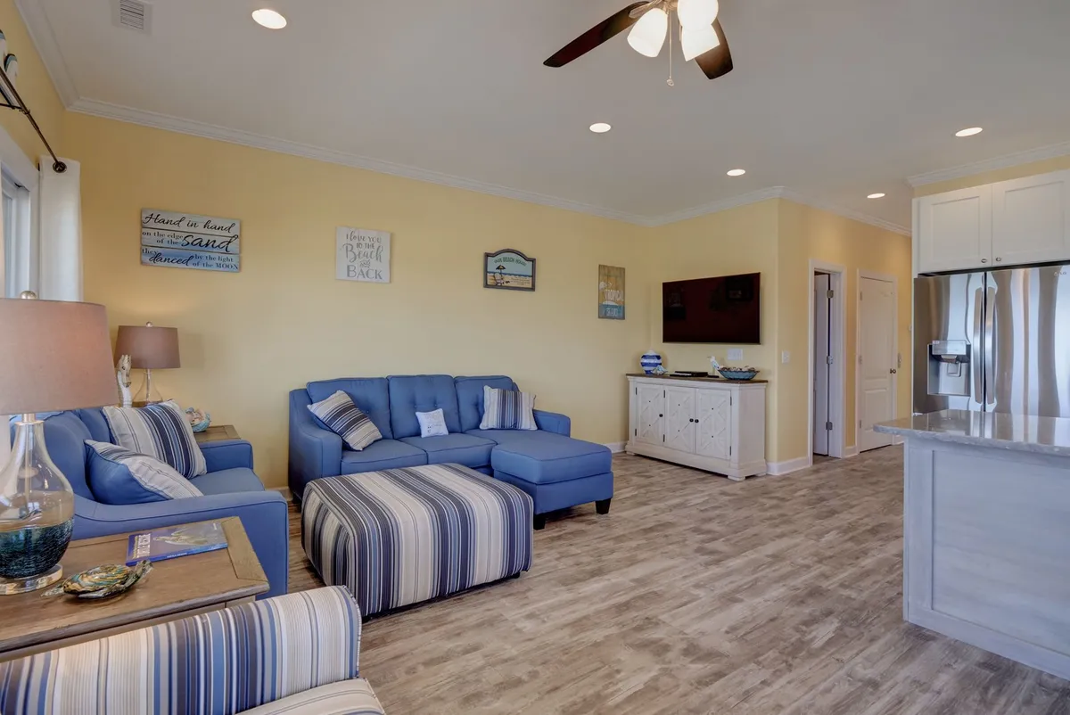 A cheerful, open-concept living space featuring a kitchen island, a blue sectional sofa, and a striped armchair. The kitchen island acts as a natural divider and gathering spot, with views into the main living area, underscoring the kitchen's central location.
