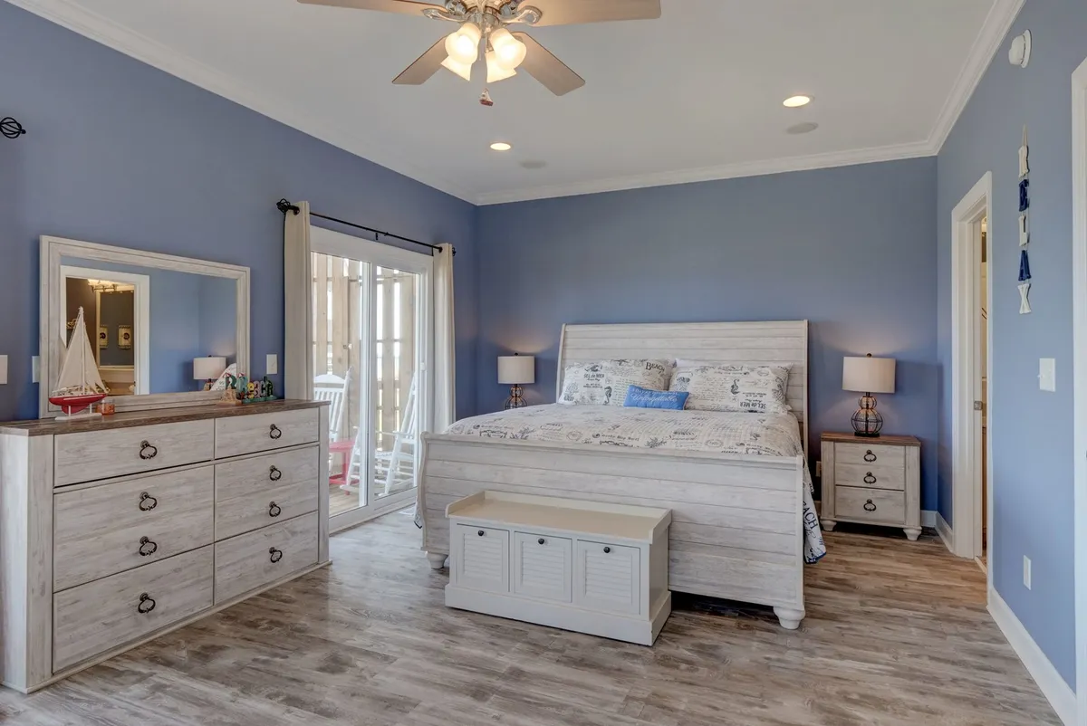 A tranquil bedroom interior featuring a bed, dresser, and sliding doors that likely open to a balcony or offer water views. The space is flooded with natural light, inviting guests to customize their stay with chosen linens and relax in a serene environment.