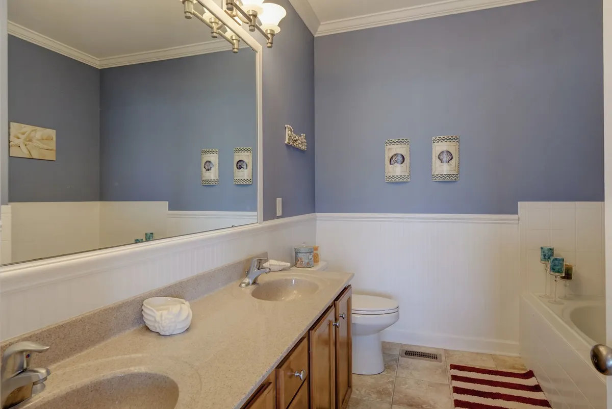 A bright, welcoming bathroom with a double sink vanity, large mirror, decorative wall art, and a bathtub with glass accents. The space is inviting and functional, ideal for both solo relaxation and busy mornings.