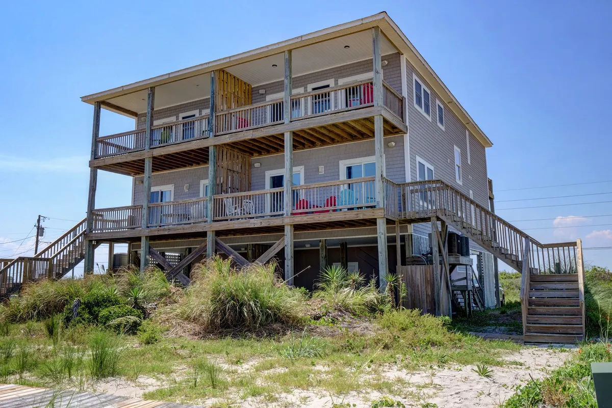 The inviting exterior of a three-story wooden duplex surrounded by natural greenery, with balconies furnished with chairs—ideal for family gatherings and outdoor relaxation. The home faces the sunrise and sunset, emphasizing access to both waterfronts.