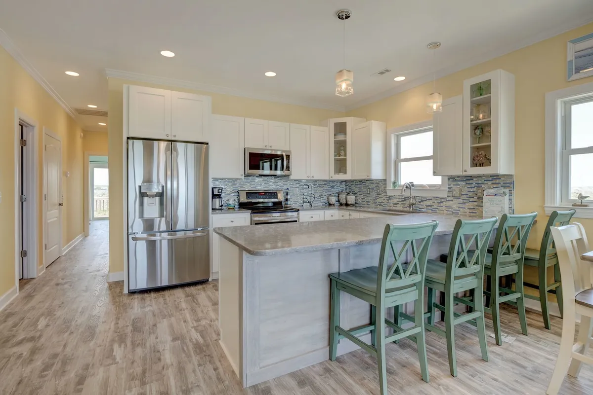 A warm and inviting kitchen scene centered on a large island countertop with bar stools, complemented by stainless steel appliances. The layout encourages both cooking and socializing, with plenty of space for guests to join in or relax at the breakfast bar.