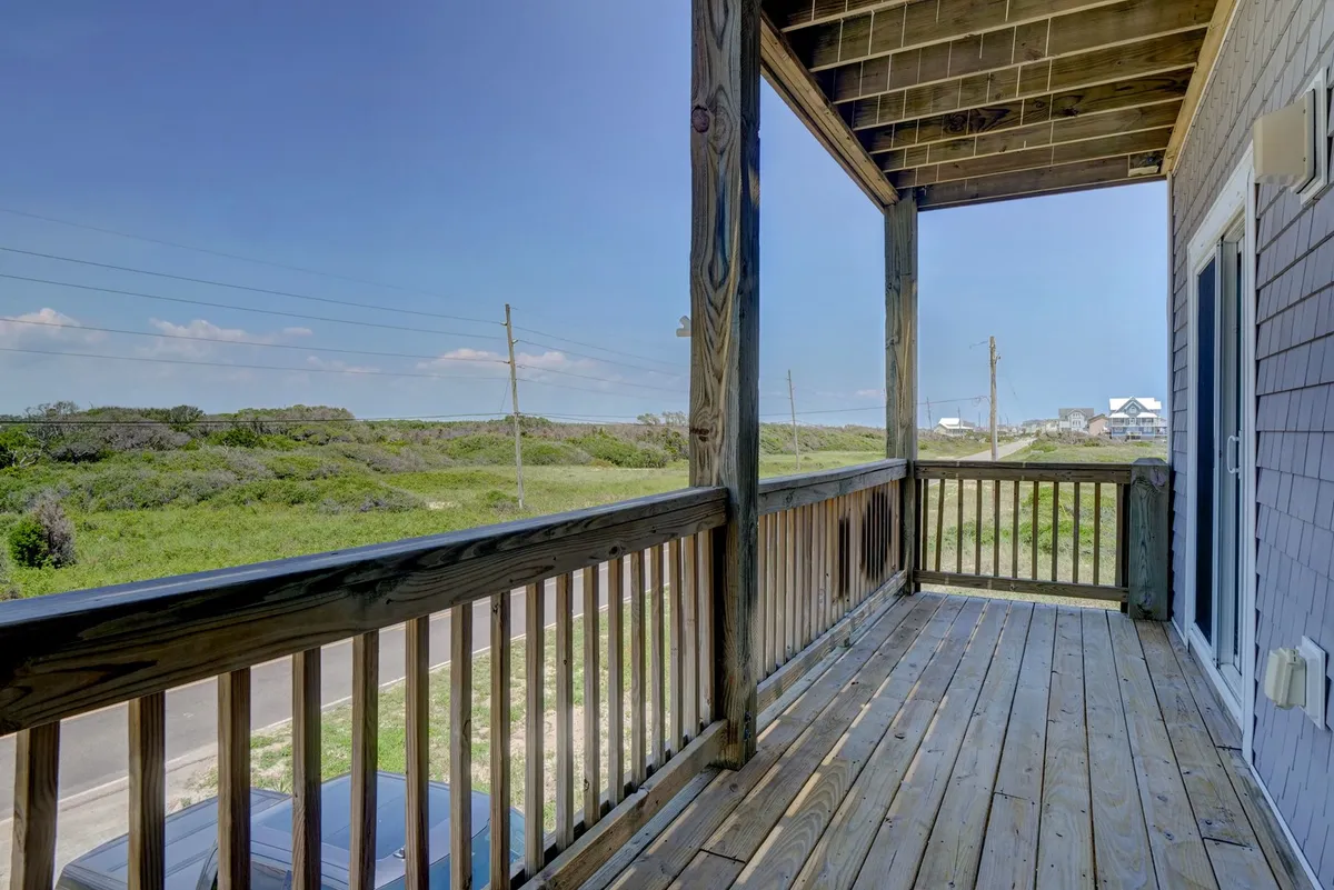 This exterior image captures a wooden balcony with open views of natural greenery, evoking a peaceful, relaxed outdoor atmosphere. The wooden railing draws the eye outward, suggesting easy access to fresh air and tranquil vistas—hallmarks of easy coastal living.