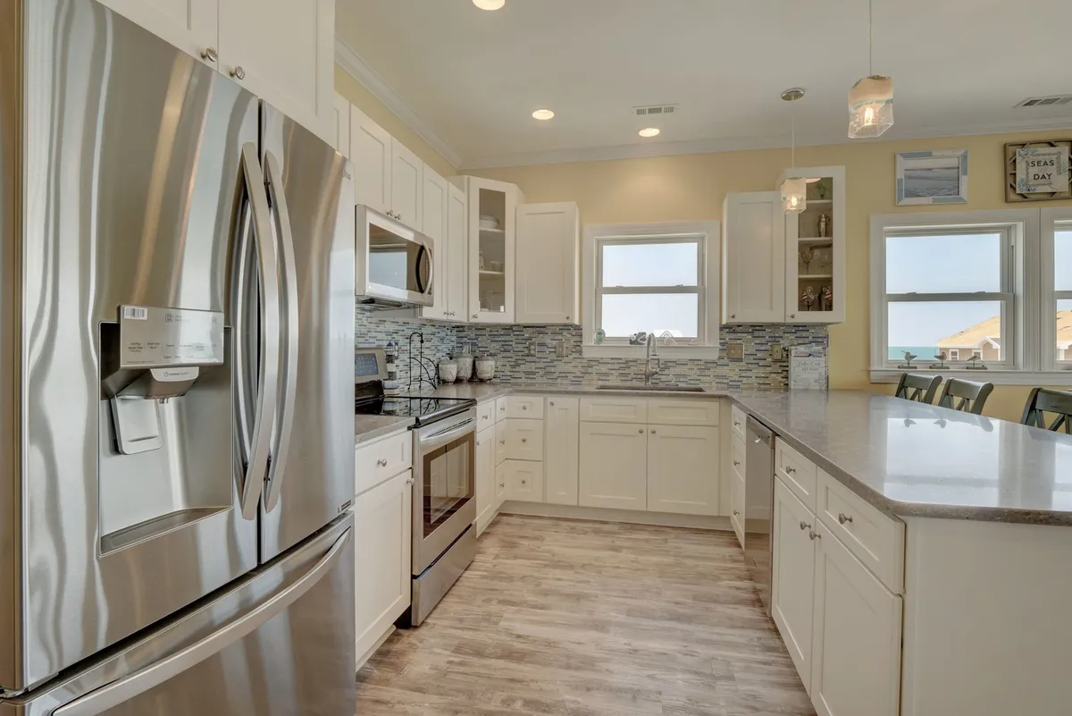 A bright, contemporary kitchen featuring gleaming stainless steel appliances, modern cabinetry, a colorful tiled backsplash, and a spacious countertop. The area is well-lit and inviting, ideal for cooking, entertaining, and group activities.